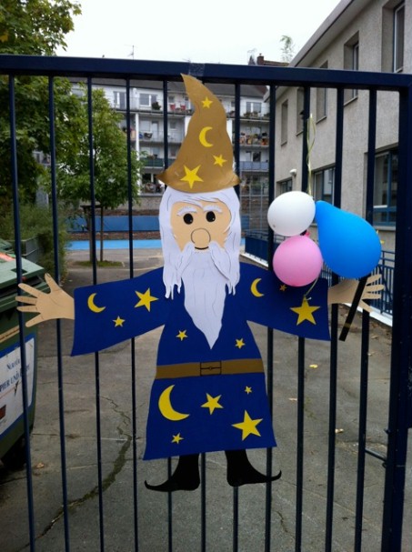Eine Zaubererfigur mit Luftballons in der Hand hängt an einem Tor.