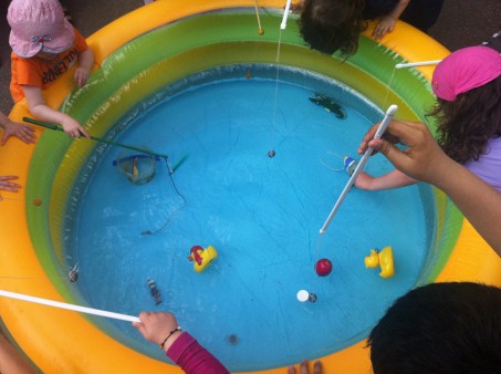 In einem Kinderplanschbecken wird von mehreren Personen nach Plastikentchen und -fischen geangelt.