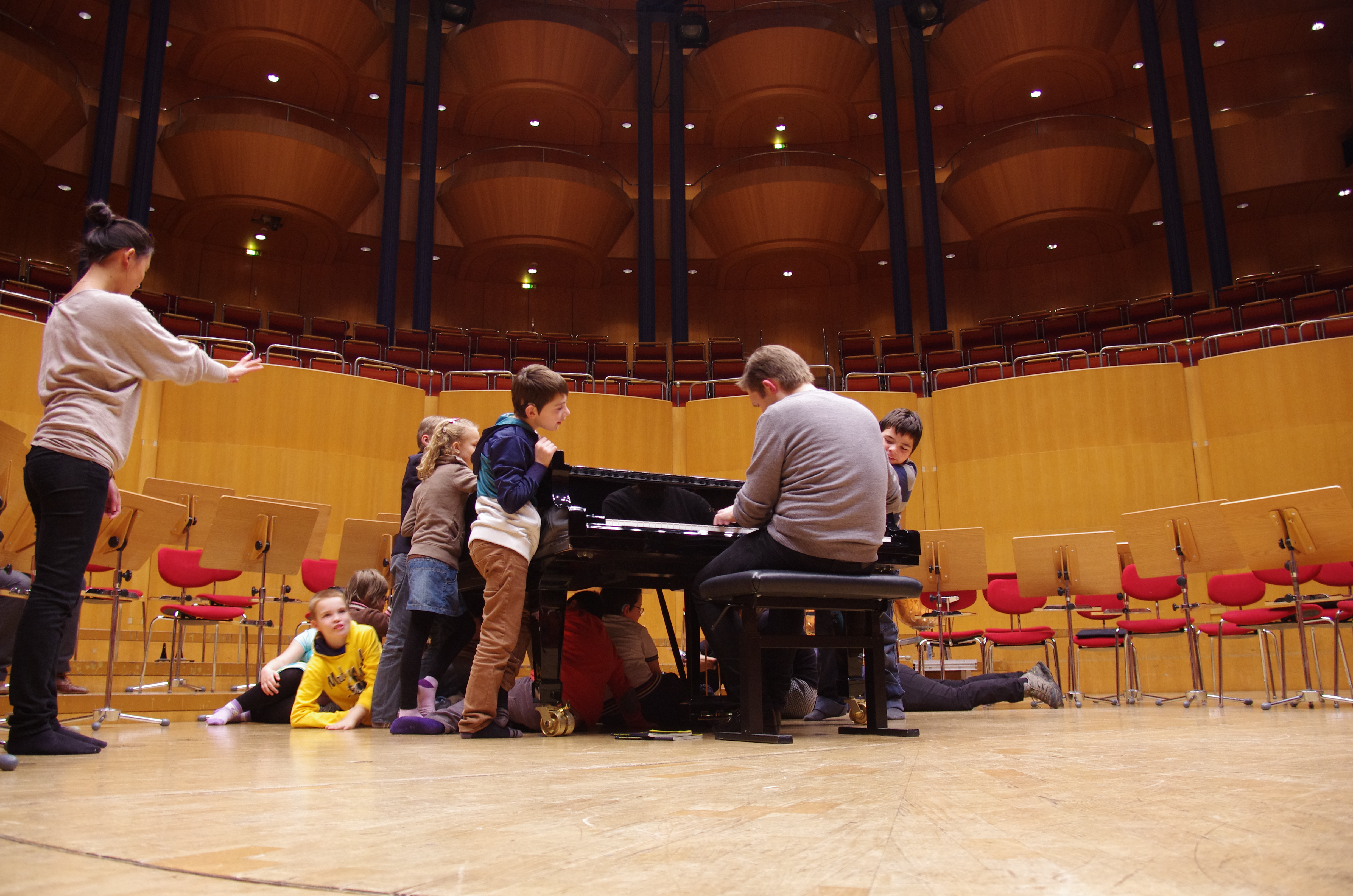 Schüler stehen um und liegen unter einem Konzertflügel in der Kölner Philharmonie